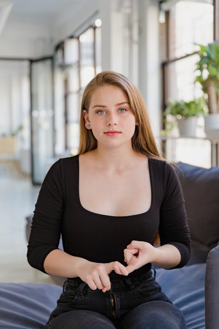 Services Portrait of a young woman gesturing sign language in a bright living room.
