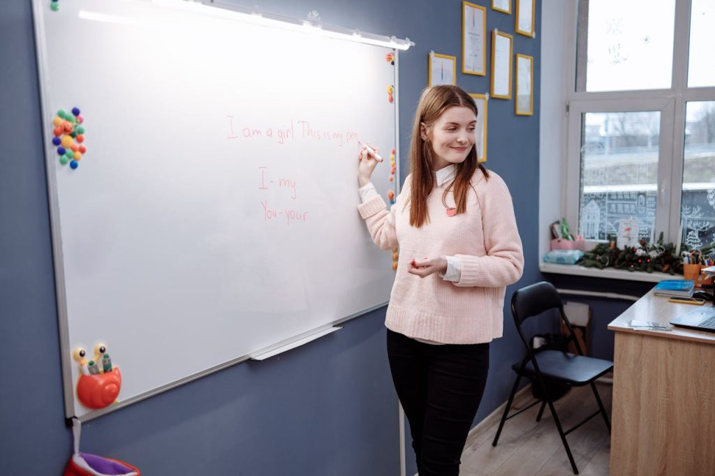 Young woman teaching Spanish lesson in a classroom, writing on a whiteboard.